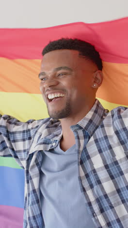 Vertical video of happy african american man holding lgbt rainbow flag, slow motion