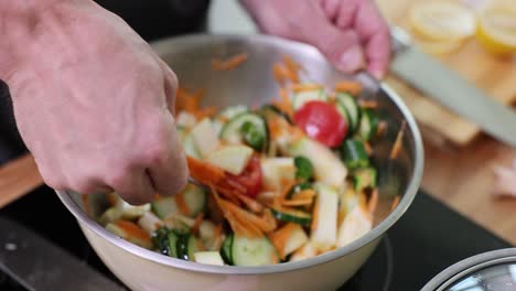 close-up of hands mixing a fresh vegetable salad in a bowl