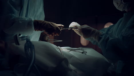 surgeons team hands suture incision in medical suit dark operating room closeup.