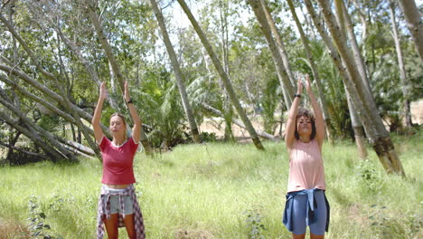 una joven caucásica y una joven biracial practican yoga al aire libre.