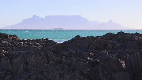 Vista-Lejana-De-La-Montaña-De-La-Mesa-Con-Olas-Del-Océano-Sobre-Las-Rocas