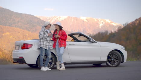 couple enjoying coffee in a convertible car on a scenic mountain road trip in autumn.