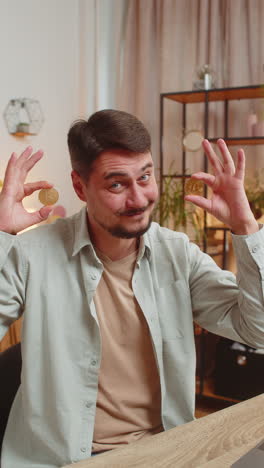 portrait of happy young male freelancer trader showing bitcoins sitting at home office table