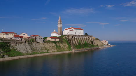 Aerial-shot-of-The-Church-of-Saint-George-standing-on-a-hill-in-Piran,-a-coastal-town-in-Slovenia