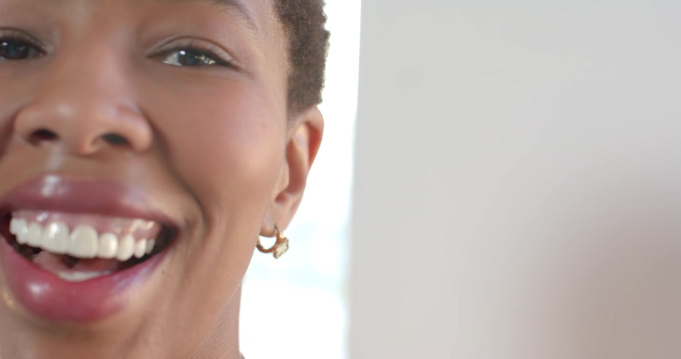 Mulher africana sorrindo e depois rindo enquanto se inclina para mais perto da câmera, usando brincos de argola de ouro e colar