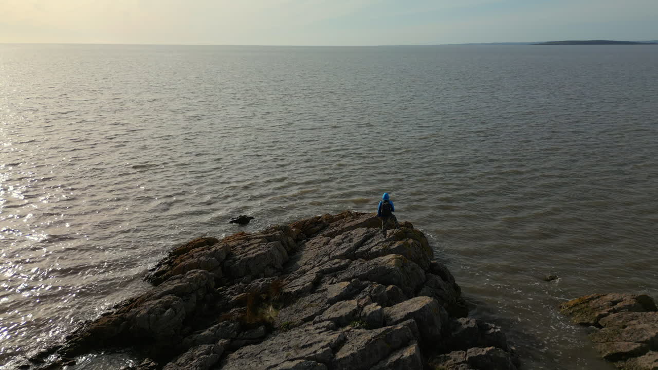 Movimento rallentato, volo sopra un escursionista su uno sperone roccioso con il mare all'orizzonte a Jenny Brown's Point, Silverdale, Regno Unito