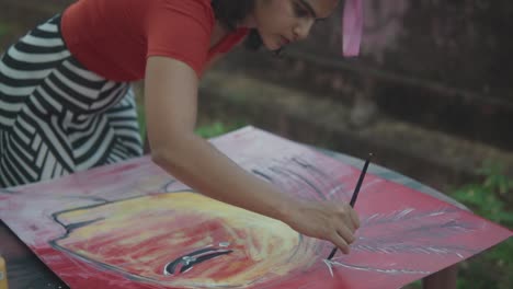 medium slow motion shot of beautiful young talented artist works on an abstract artwork while she draws lines with the brush with white paint in garden