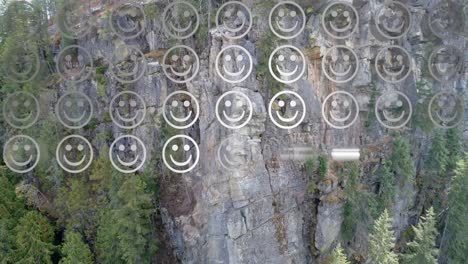 Digital-composition-of-rows-of-multiple-smiling-face-emojis-against-aerial-view-of-a-mountain