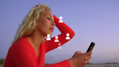 animation of multiple profile icons floating over caucasian woman using smartphone near the sea