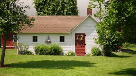 static shot of a white building with a red door on a farm on a sunny day