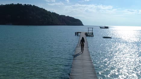 female walking alone on a pier in the ocean on a tropical island, koh kood, thailand