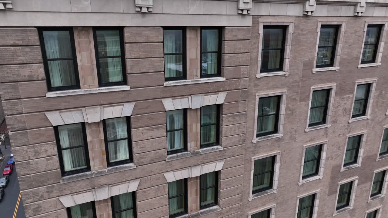 Toma aérea con dron ascendiendo por la fachada de un edificio de apartamentos en el centro de una ciudad estadounidense, revelando hileras de ventanas y arquitectura urbana clásica en un denso distrito metropolitano