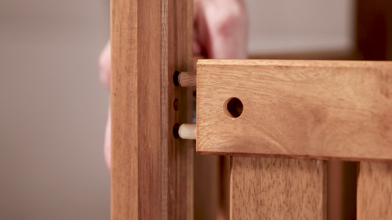 Hands assembling wooden furniture using dowels in a softly lit environment. Close-up view highlights precision and craftsmanship
