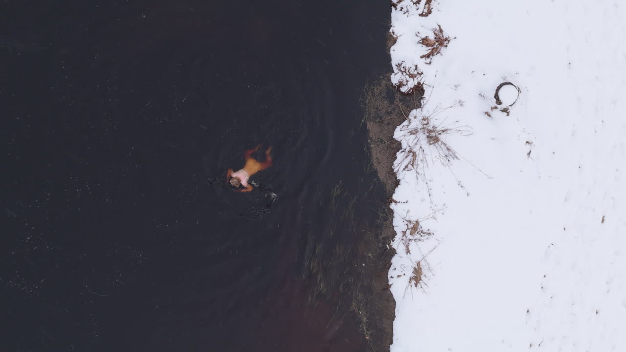 Snow falls around the female ice bather, winter in Sweden aerial plan view