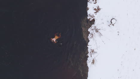 Snow-falls-around-the-female-ice-bather,-winter-in-Sweden-aerial-plan-view