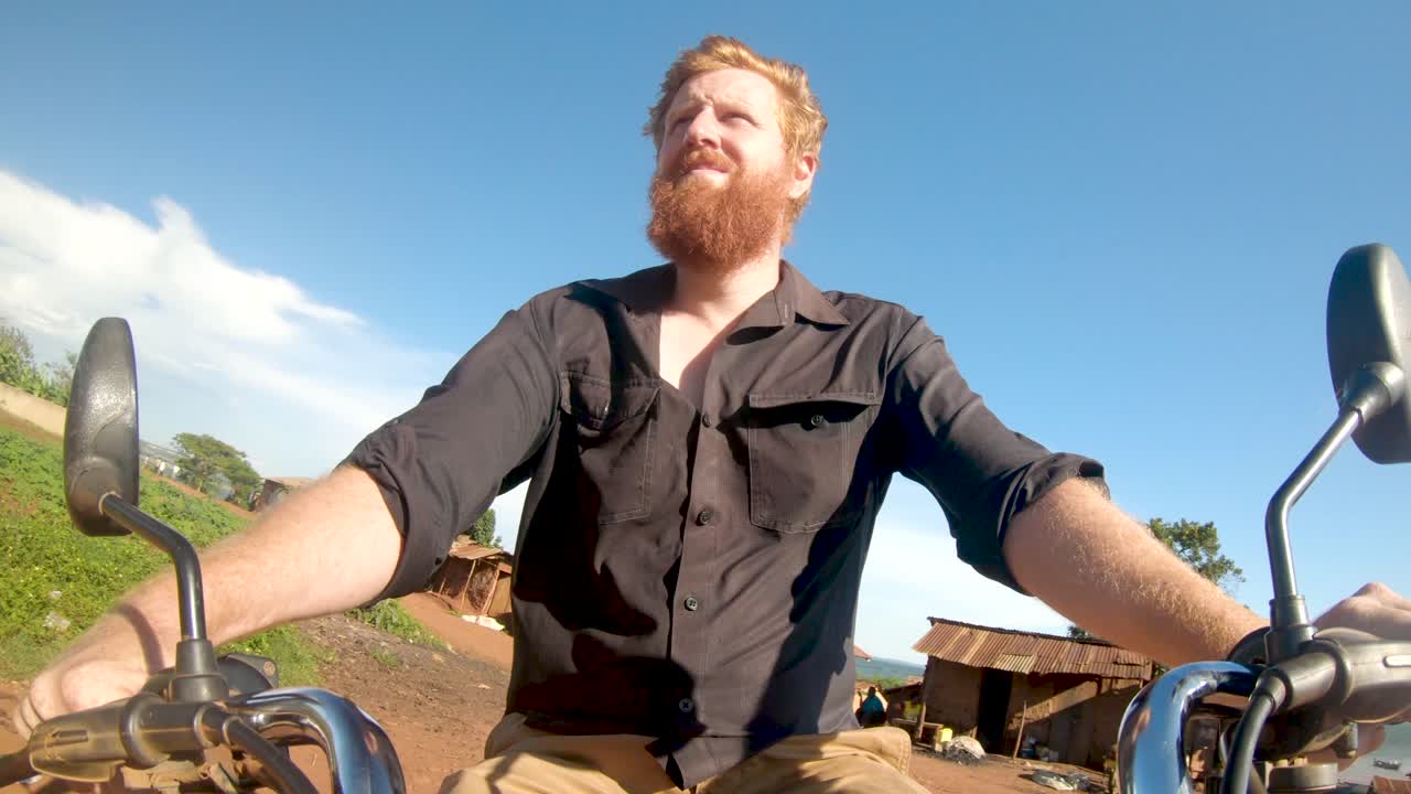 Redhead Man Driving a Motorbike Through an African Village