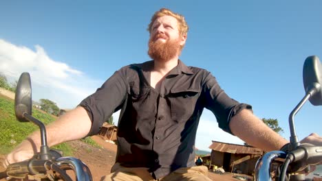 redhead man driving a motorbike through an african village