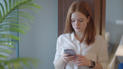 young woman is hiding in office hall with smartphone sending message and viewing social media