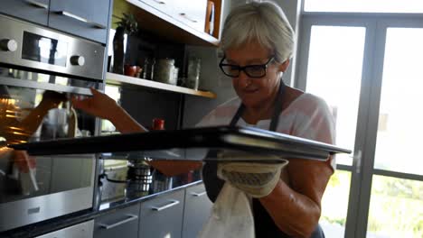 senior woman removing cookie tray from oven 4k