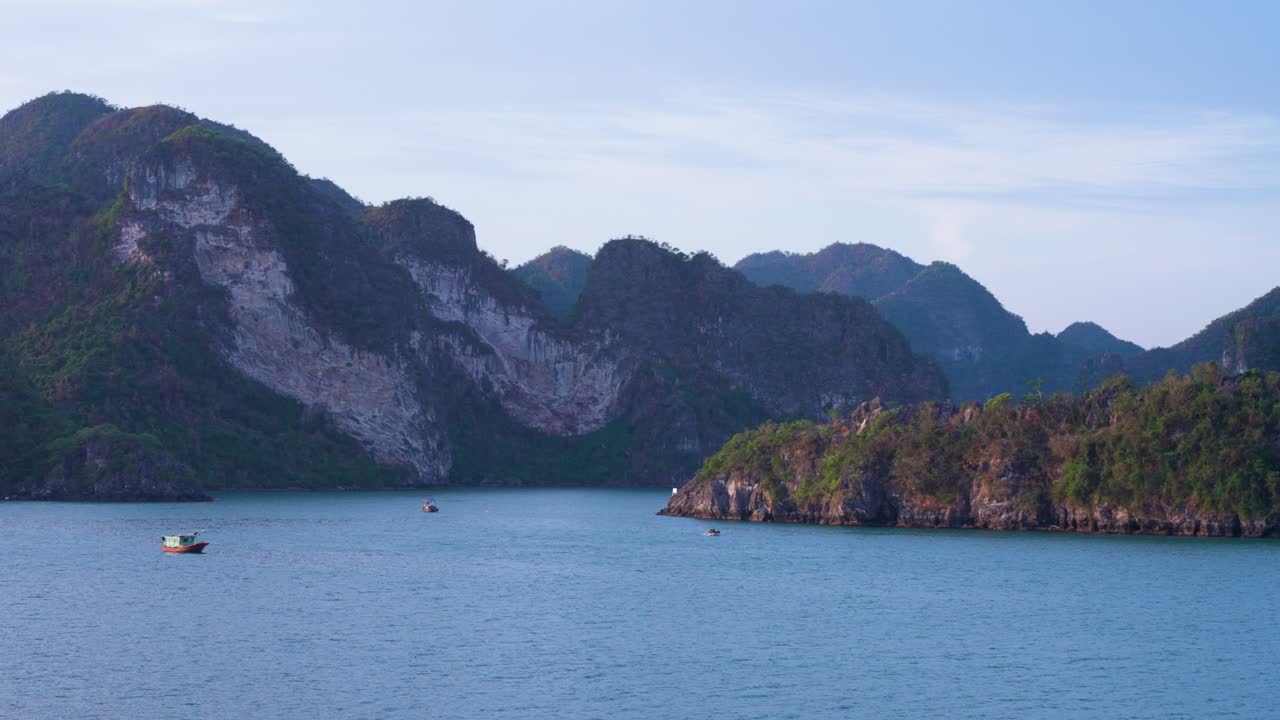 Ha Long Bay's iconic limestone karsts rising dramatically from turquoise waters, with steep cliffs and forested peaks creating a majestic backdrop while small fisherman's boat navigate tranquil bay
