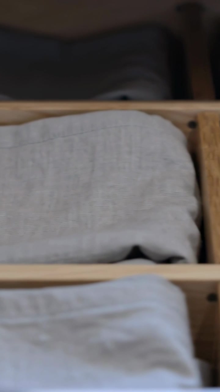 Vertical video: Shifting camera revealing folded linen stack in wooden drawer, showing neat order