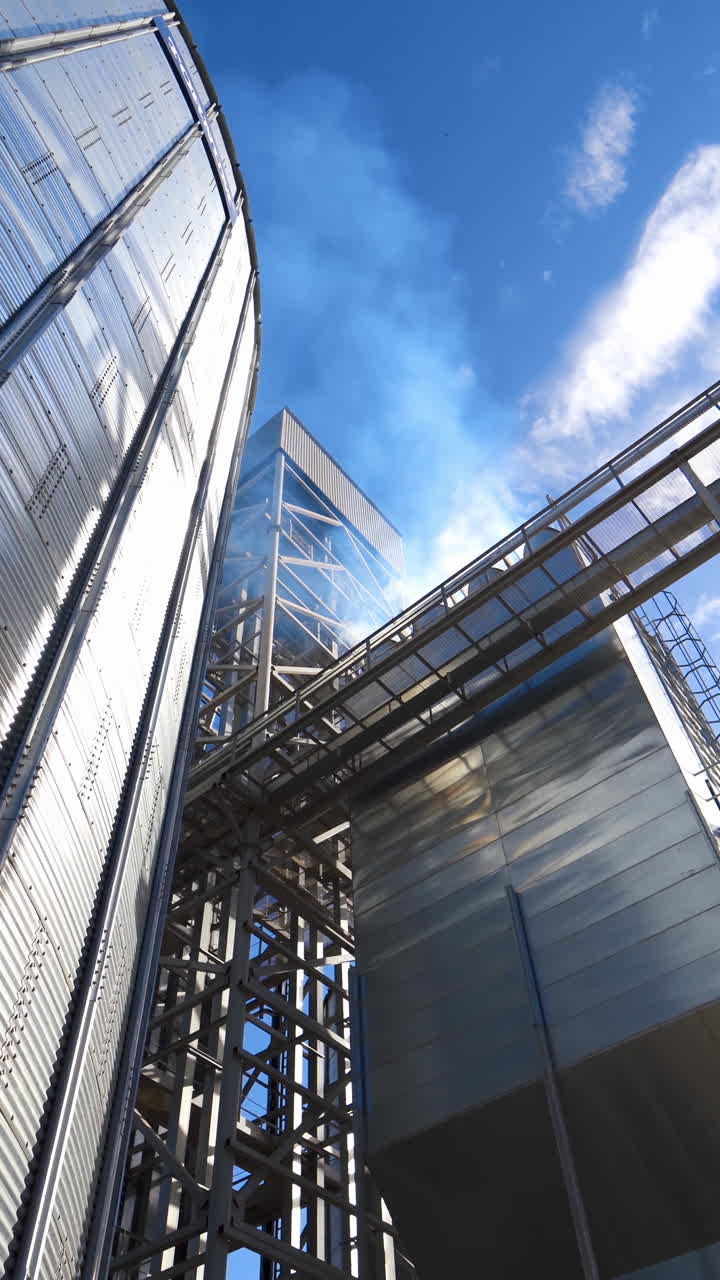 Silver grain elevator in sunny weather. Metal construction of a large industrial plant. Granary for storage and processing agricultural products. Close-up. Vertical video