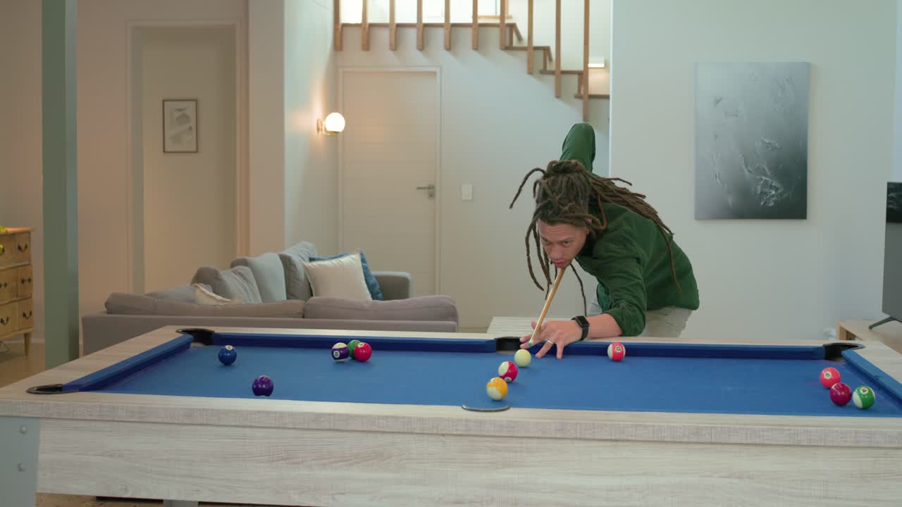 Surveying balls and adjusting cue stick, man striking cue ball and grinning at home pool table