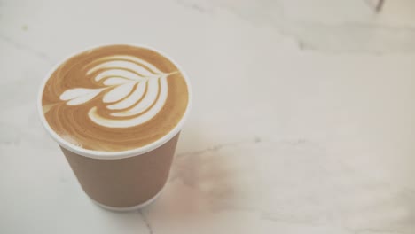 Handheld-top-down-view-of-disposable-compostable-cup-with-coffee-and-latte-art-flower