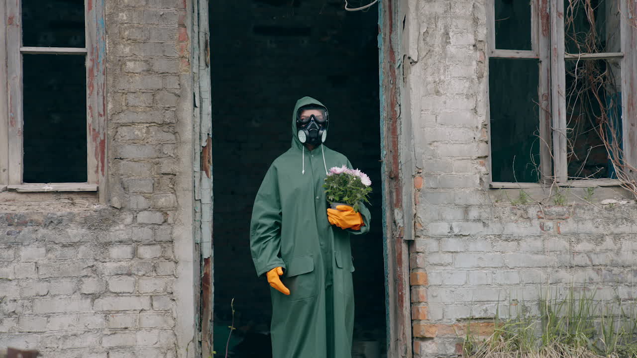 Person at post-apocalyptic place. Man in protective suit with flowers in abandoned place after ecological disaster. Emission of radiation.