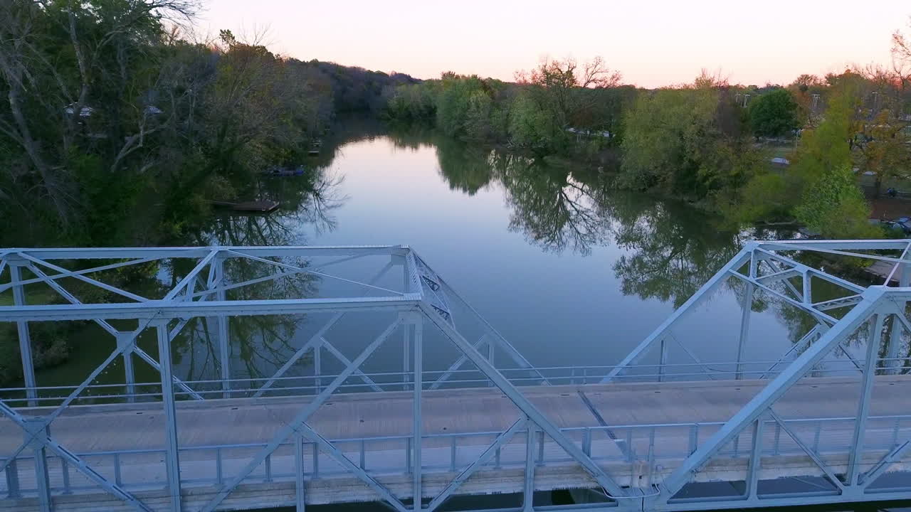 Drone flying above a river in Missouri toward a dam and bridge before rising over and passing the bridge in smooth cinematic HD footage during golden hour with peaceful scenic views