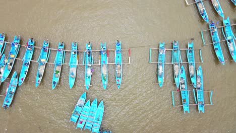 Aerial-view-pulling-back-of-baby-blue-outrigger-fishing-boats-anchored-in-harbor,-Indonesia