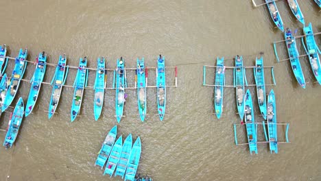 aerial view pulling back of baby blue outrigger fishing boats anchored in harbor, indonesia