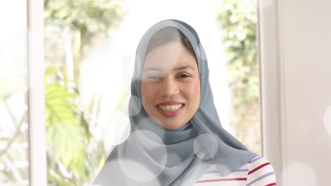 animation of leaves over biracial woman in hijab smiling