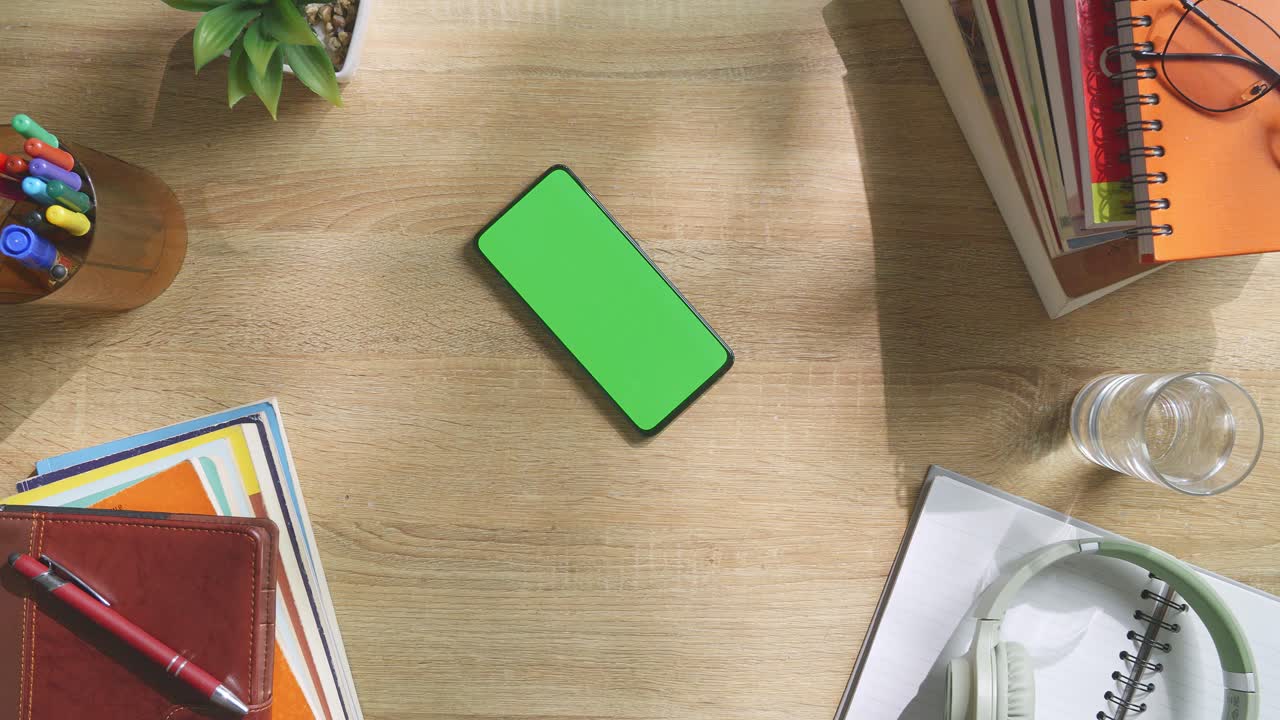 vista de arriba hacia abajo de una computadora portátil con pantalla verde simulada pantalla chromakey en un escritorio de oficina de madera al lado de la libreta con bolígrafos, gafas y un vaso de agua.