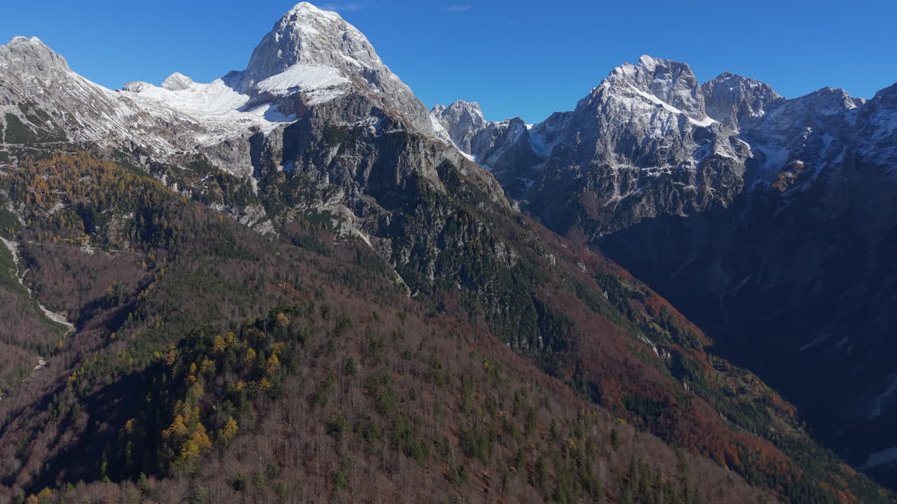 Julian Alps aerial flight with snow mountains and autumn forest. Slovenia