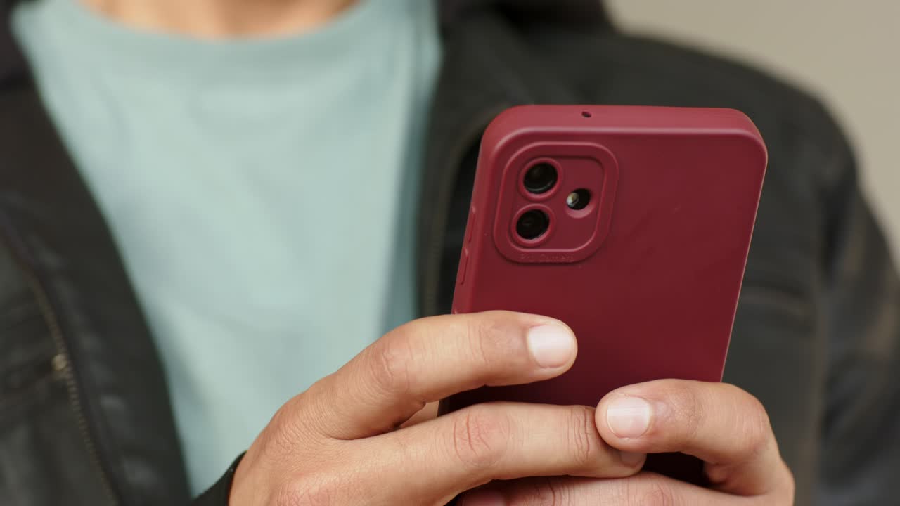 Un uomo sta usando il pollice su uno smartphone rosso in una stanza, toccando l'angolo destro per scorrere e controllare le notifiche