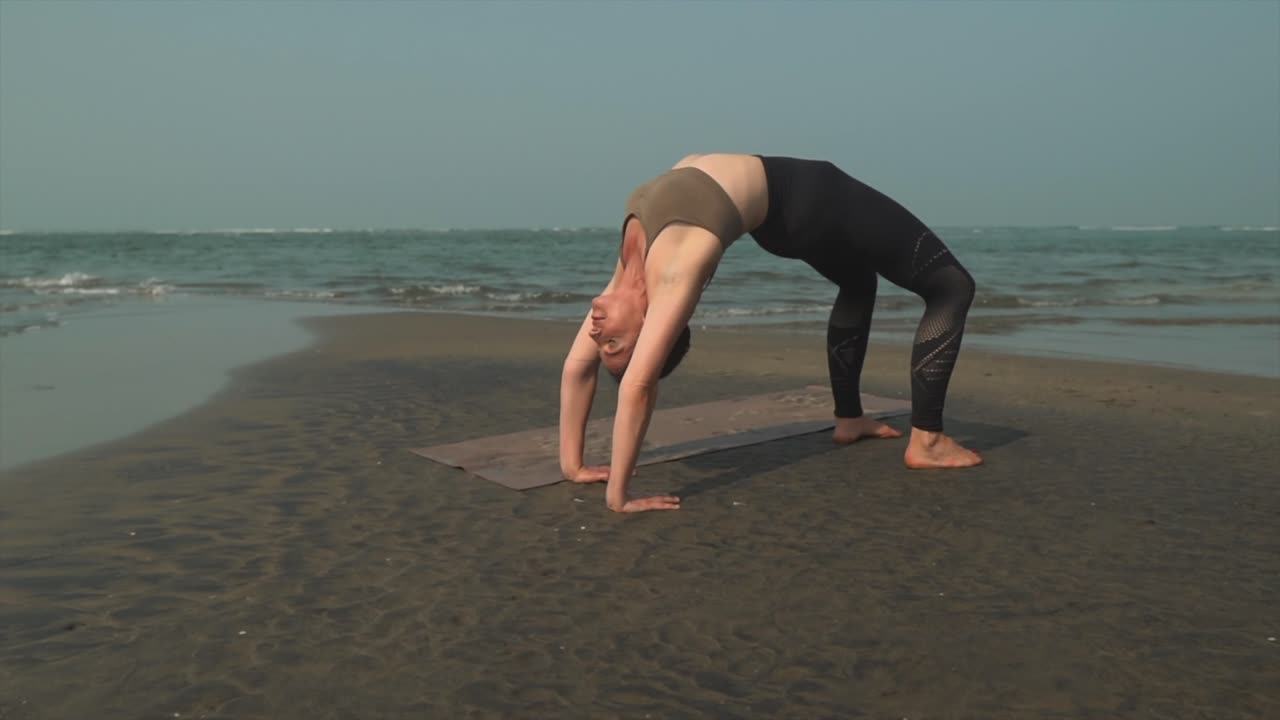 mujer de yoga caucásica en pantalones de chándal se estira hacia atrás en una playa tranquila
