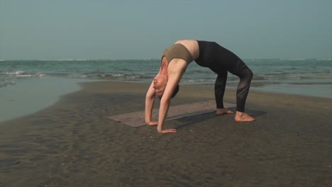 caucasian yoga woman in sweatpants stretches backwards on calm beach