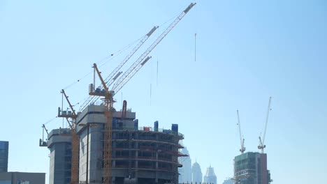 tilt up panorama of huge construction cranes are in unfinished building in big modern city