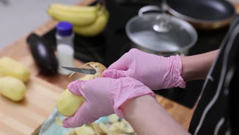 hands in pink gloves peeling a potato