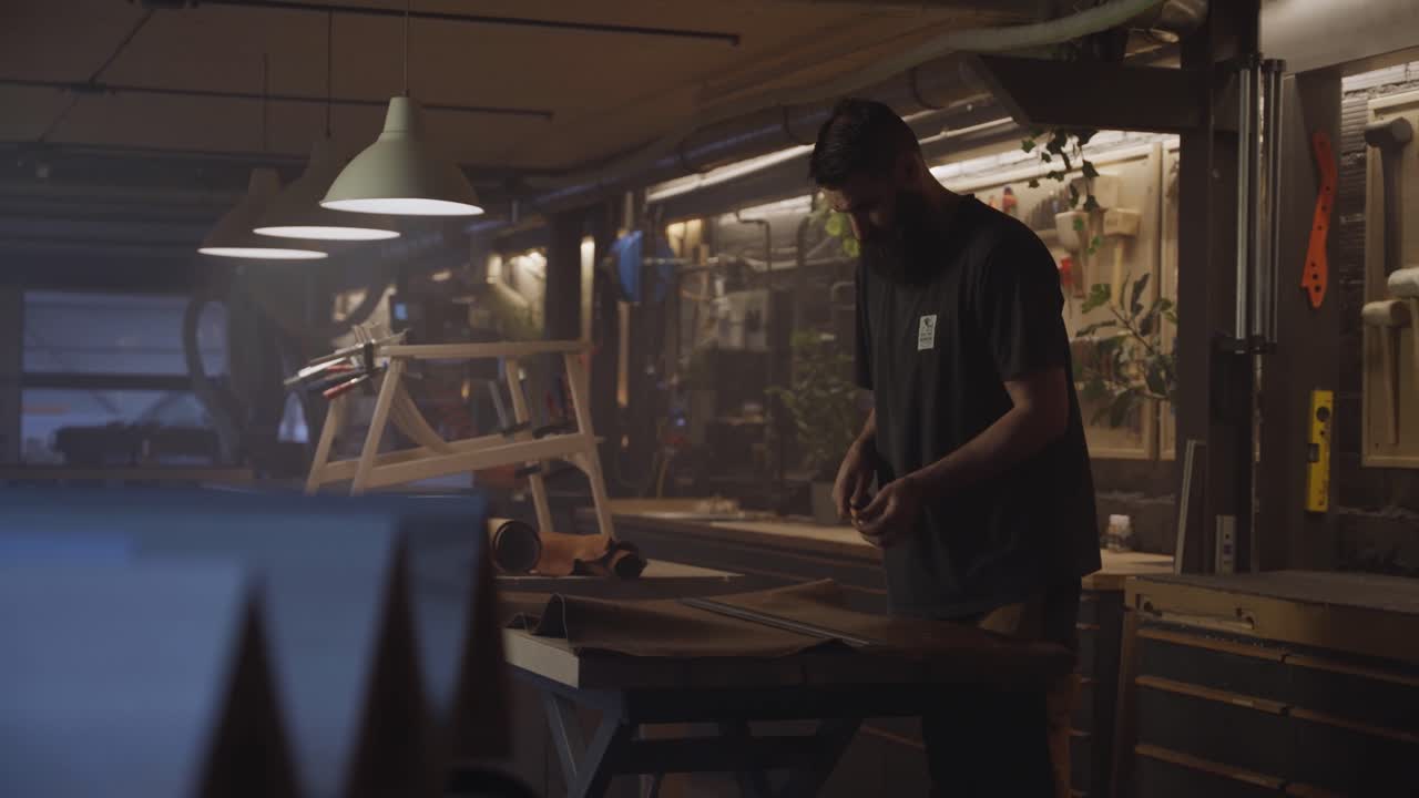 A craftsman works carefully with a large sheet of leather in a workshop filled with tools, showcasing precision, craftsmanship, and traditional leatherworking techniques