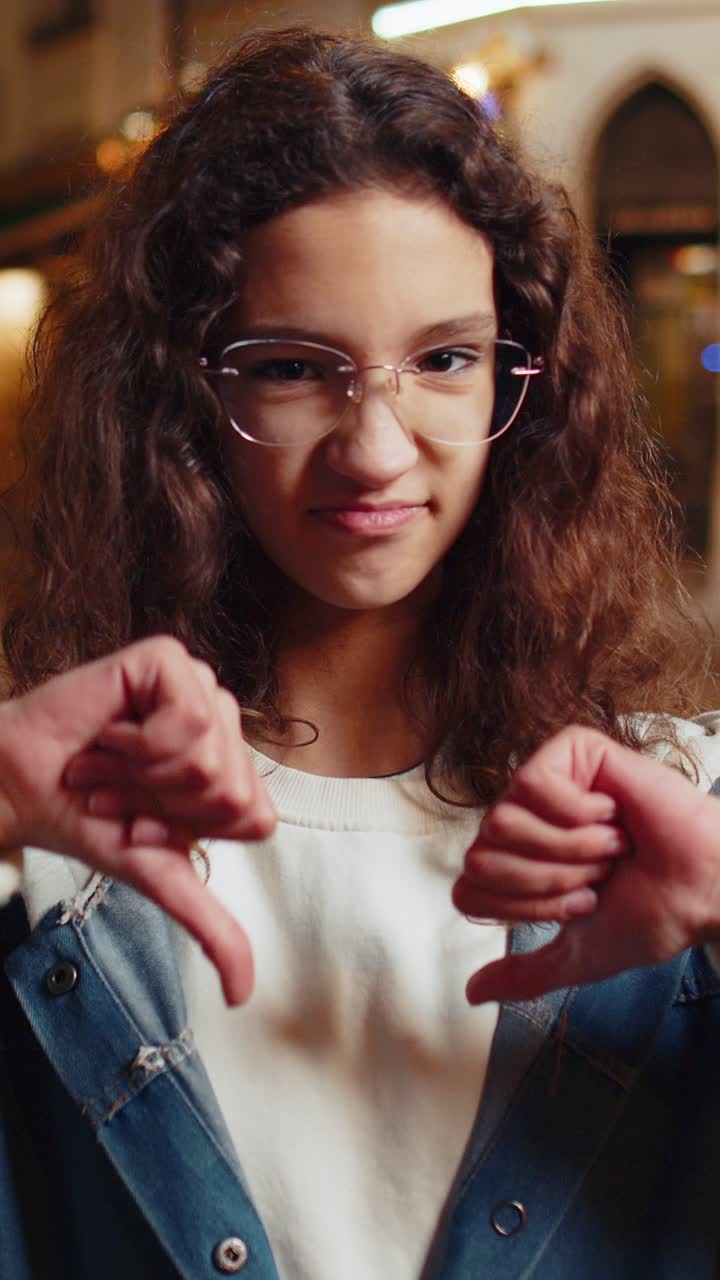 Upset teenage girl child showing thumbs down dislike sign gesture expressing discontent disapproval