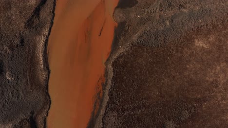 aerial top-down view of the yellow river merging with the þjórsá river in iceland, creating a striking contrast between the earthy brown terrain and the vibrant orange water.