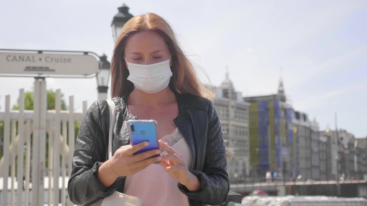 hermosa mujer rubia con máscara y teléfono celular en amsterdam, países bajos - pandemia de coronavirus - tiro medio, cámara lenta