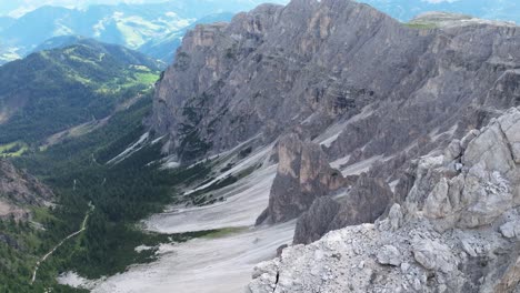 Aerial-view-of-the-Dolomites-showcasing-the-dramatic-cliffs-and-verdant-valleys-below,-with-imposing-rock-formations-in-the-foreground