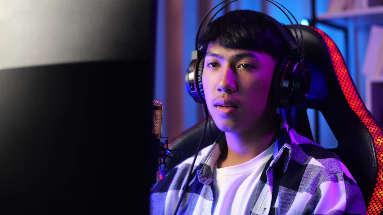 primer plano de un chico asiático que se estira mientras juega un juego a través de la red en una computadora personal. videojuego de transmisión en vivo, escritorio iluminado por luz de tira led rgb