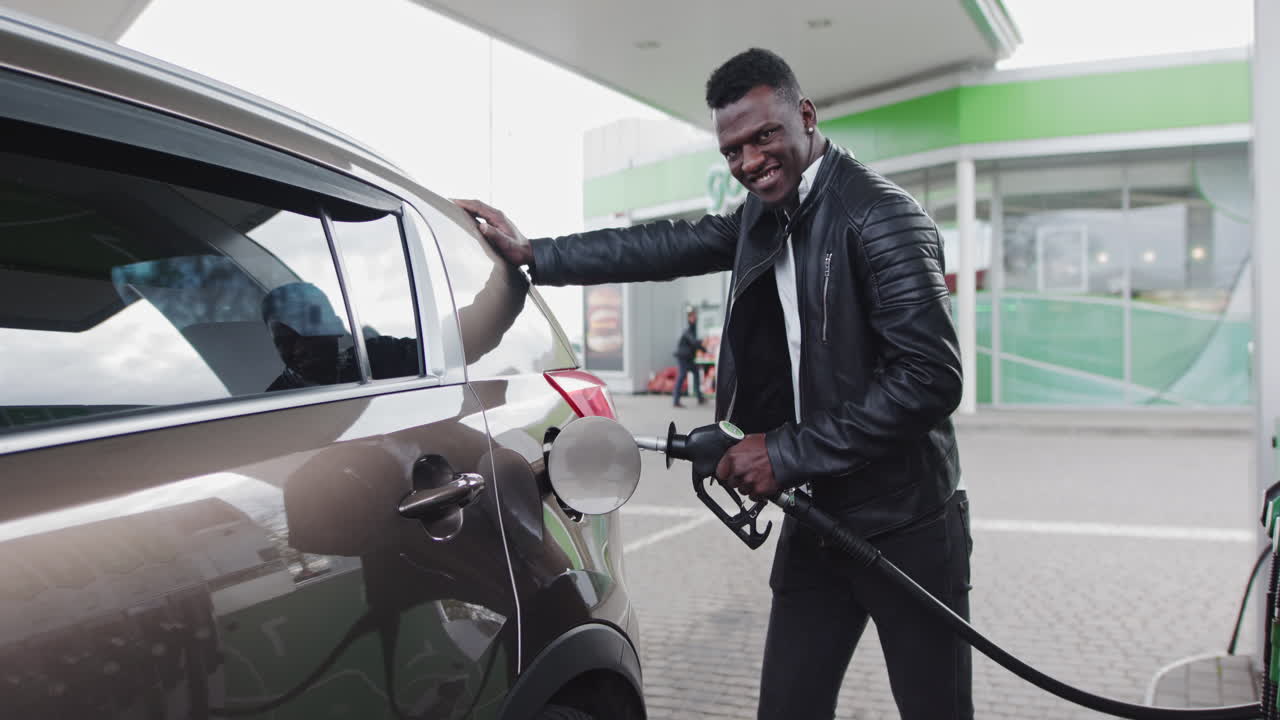 Uomo afroamericano alla moda alla stazione di servizio vicino alla sua jeep; l'uomo fa rifornimento alla sua auto e guarda