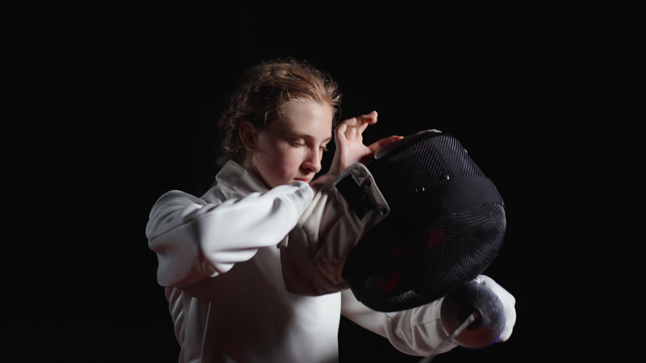 젊은 여성 펜싱 선수가 스튜디오에서 칼을 들고 포즈를 취하고 있습니다.