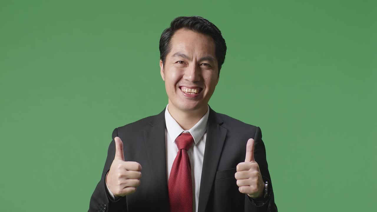 아시아 사업가 한 명 이 그린 스크린 스튜디오 에 서 있는 동안 엄지손가락 을 올려 놓고 미소 를 지고 있다