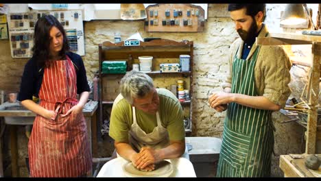 Colleagues-looking-at-potter-while-making-a-earthen-pot-on-a-pottery-wheel